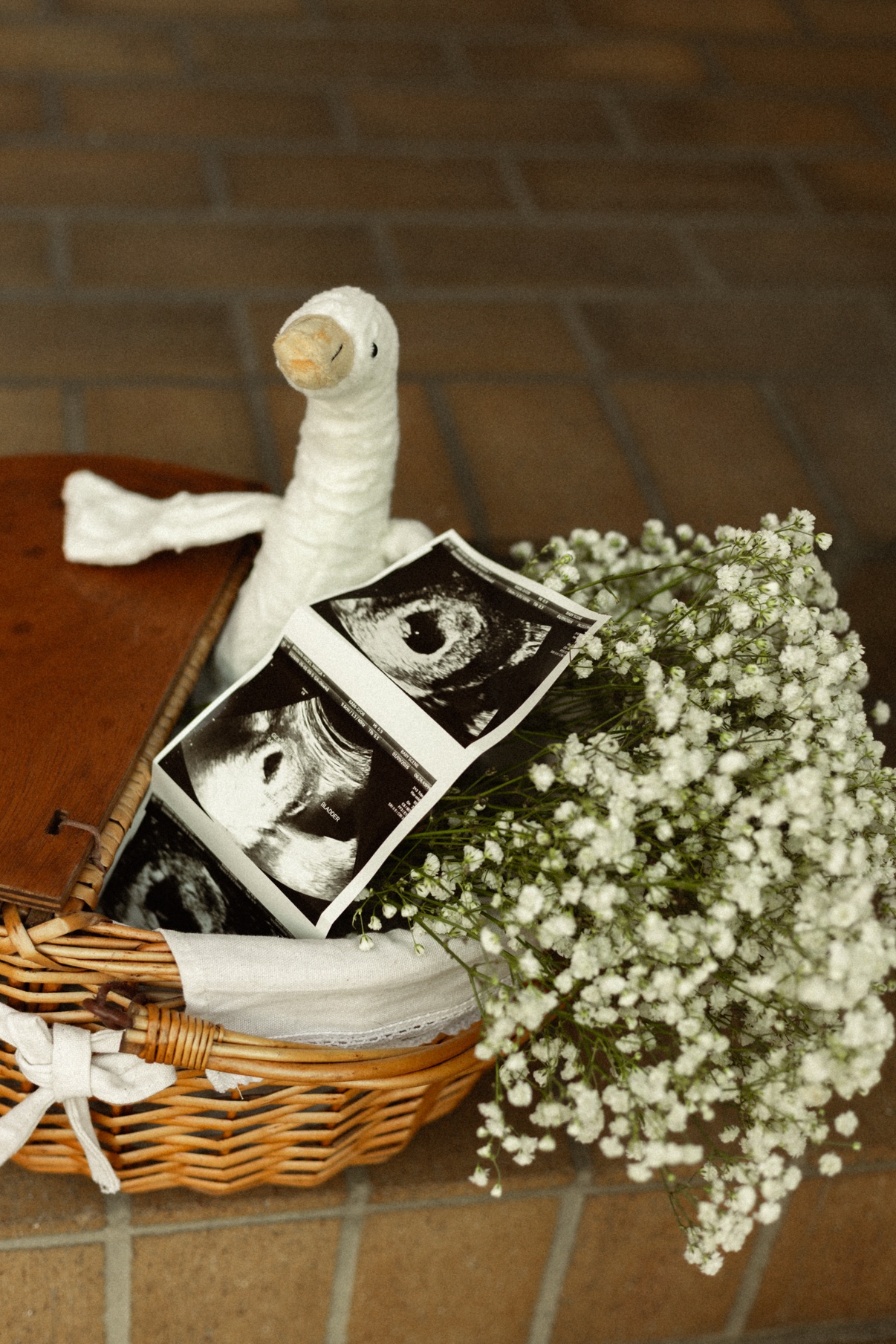 Baby's breath spilling from a woven basket beside ultrasound prints