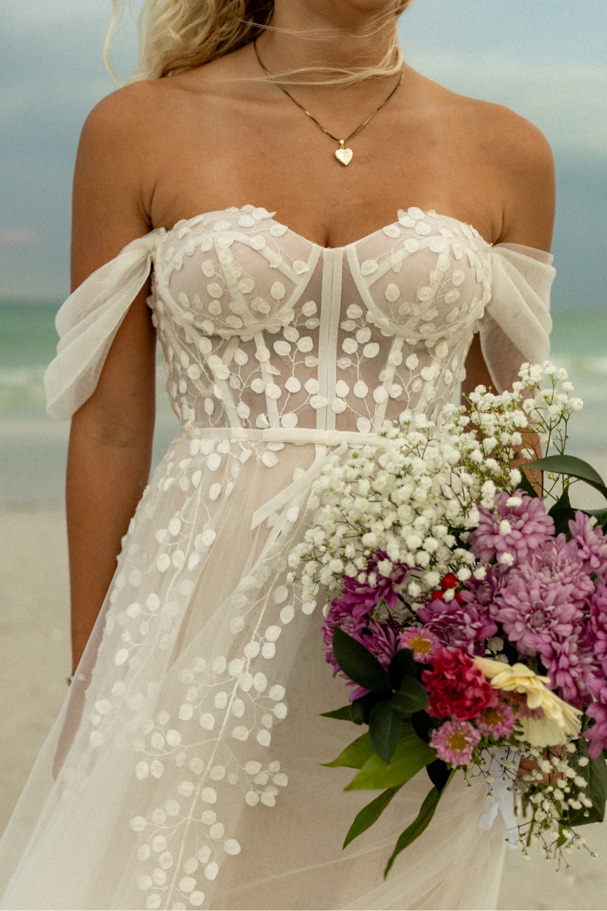 Bride on the beach holding a colorful bouquet of baby's breath, chrysanthemums, and roses