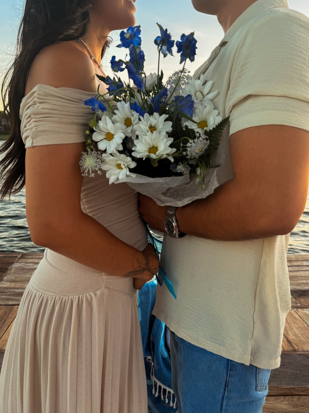 Couple holding a blue and white daisy bouquet together at sunset