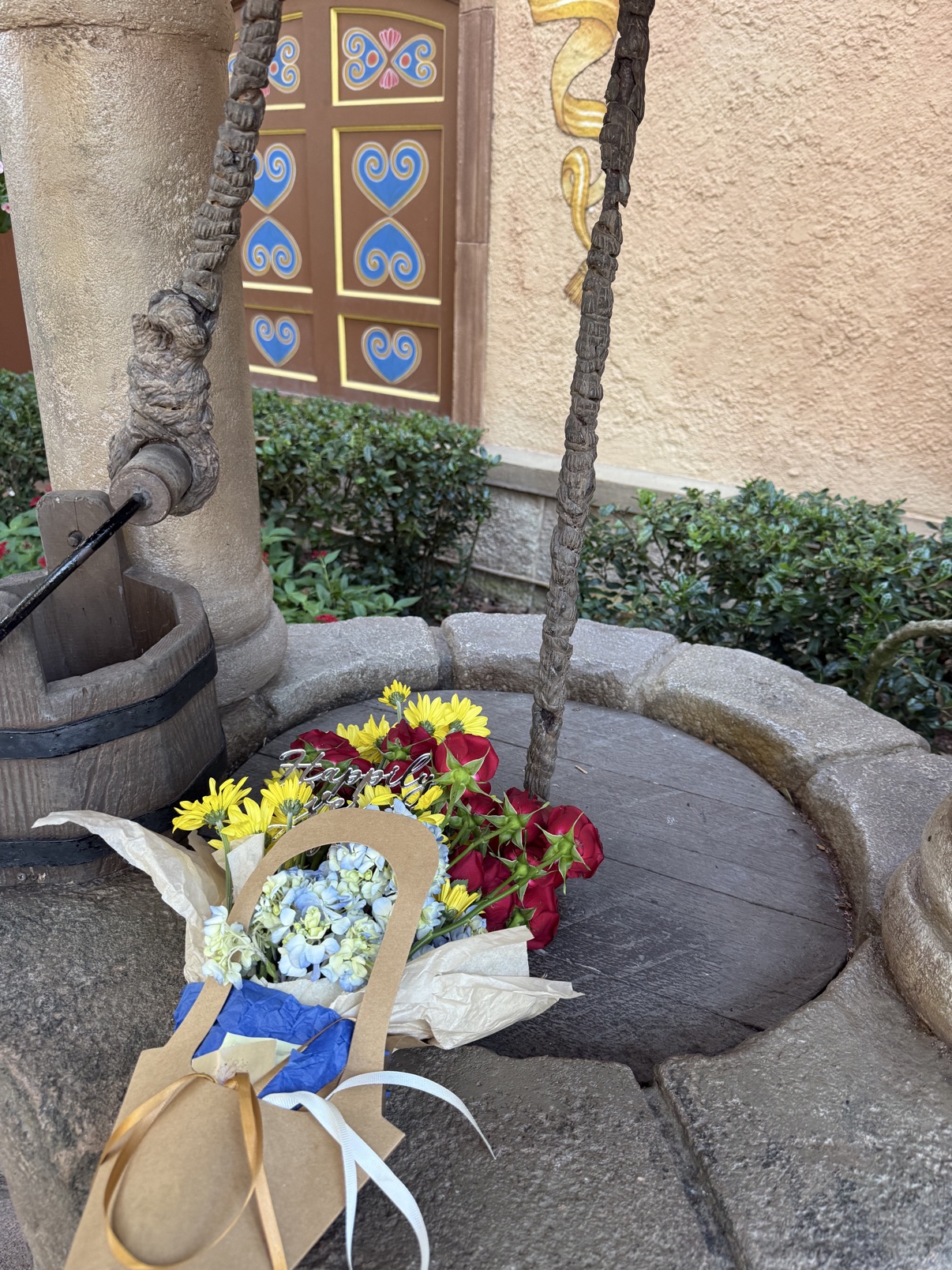 The Fairest One bouquet on Snow White's wishing well at EPCOT's Germany pavilion, with the pavilion's painted door behind it