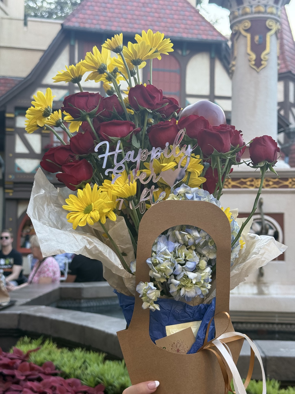 The Fairest One bouquet held up in front of the half-timbered buildings of EPCOT's Germany pavilion