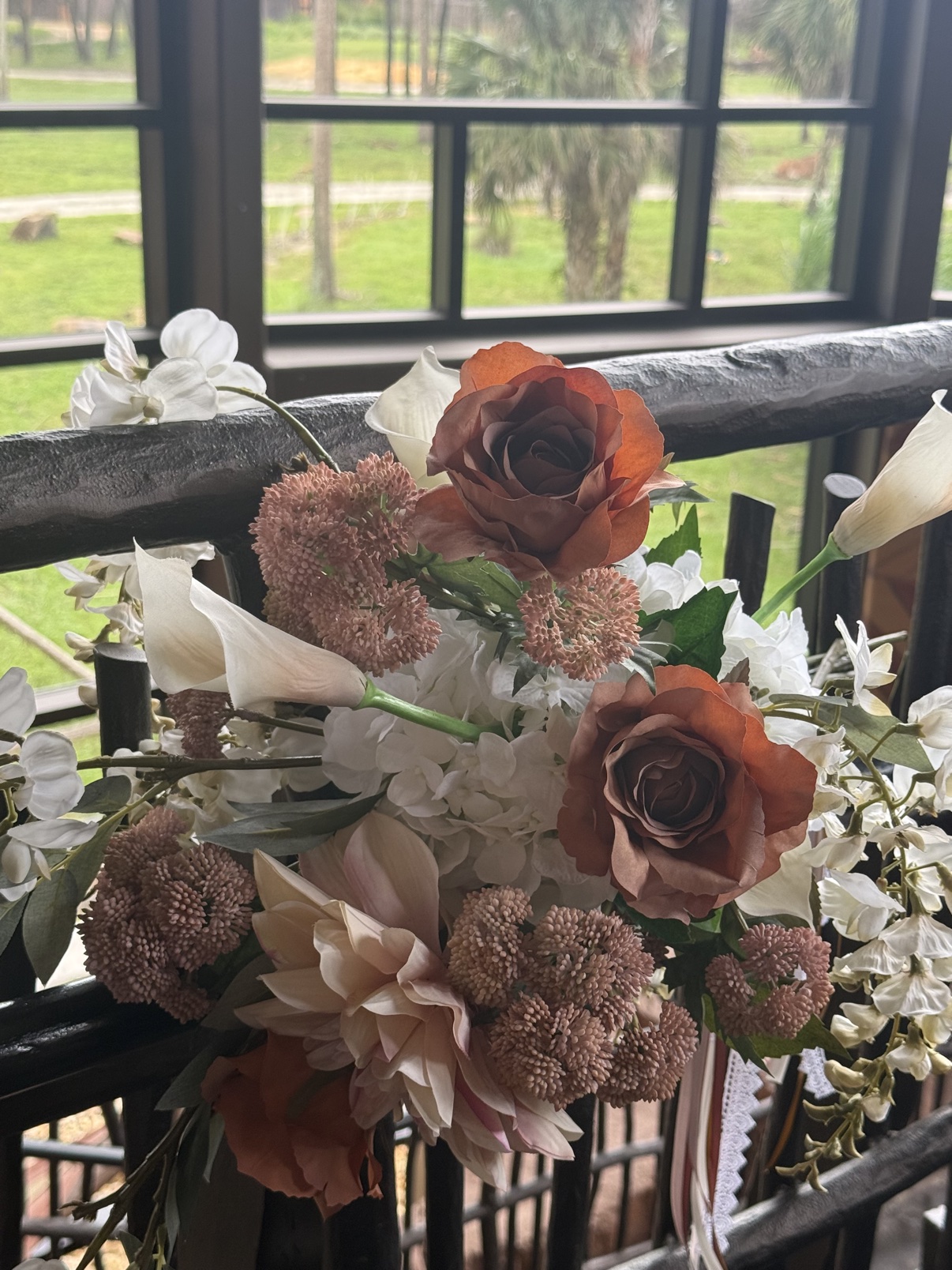 Close-up of rust roses, a blush dahlia, and white calla lilies in the custom faux Victorian Grande bouquet