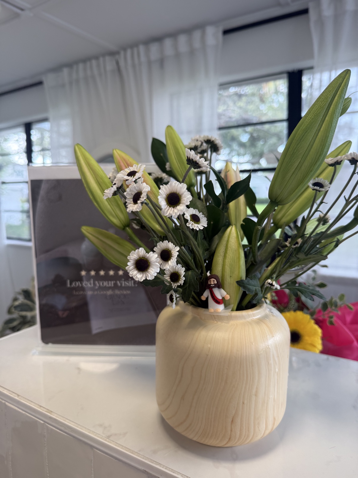 White lilies and daisies arranged in a cream vase for an event